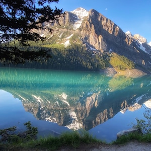May include: A mountain lake with a clear blue sky and a reflection of the mountains in the water. The lake is surrounded by trees and mountains.
