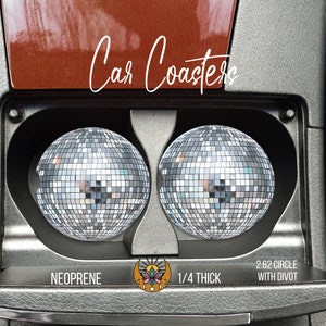 May include: Two silver disco ball car coasters with a black and silver holder. The coasters are 2.62 inches in diameter and 1/4 inch thick. The text "Car Coasters", "NEOPRENE", "1/4 THICK", and "2.62 CIRCLE WITH DIVOT" is printed on the holder.