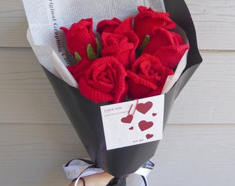 Könnte beinhalten: Ein Strauß roter gehäkelter Rosen, verpackt in schwarzem Papier mit einer weißen Karte, auf der "Love You" steht und rote Herzen abgebildet sind. Der Strauß ist mit einem weißen Band gebunden, auf dem das Wort "LOVE" steht.
