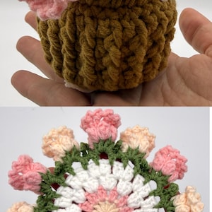 May include: A crochet flower arrangement featuring a cluster of light pink and cream-colored blossoms emerging from a textured brown pot, alongside a flat, circular crochet coaster with a white and pink center surrounded by green leaves and pink flowers.