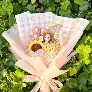 May include: A handmade bouquet with crocheted flowers in pink, yellow, and brown, wrapped in pink paper and tied with a ribbon that says "LOVE IS ETERNAL". The bouquet includes a crocheted doll.