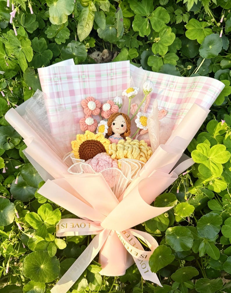 May include: A handmade bouquet with crocheted flowers in pink, yellow, and brown, wrapped in pink paper and tied with a ribbon that says "LOVE IS ETERNAL". The bouquet includes a crocheted doll.