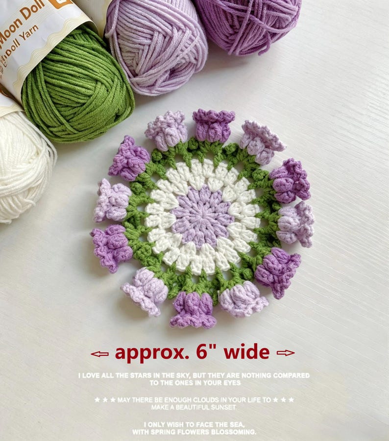 May include: A round crochet doily featuring a white center, a light purple inner ring, and a green outer border adorned with twelve small, three-dimensional purple tulip-shaped flowers. The text below states approx. 6" wide.