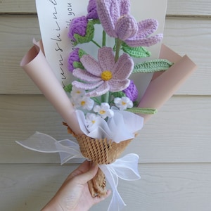 May include: A handmade crochet bouquet with lavender, light purple, and white flowers and green leaves. The bouquet is wrapped in pink and brown paper, tied with a white ribbon, and includes a card that says "sunshine with you."