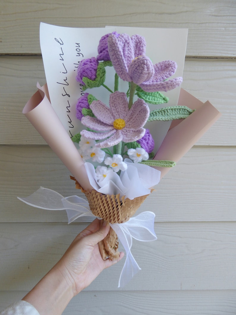 May include: A handmade crochet bouquet with lavender, light purple, and white flowers and green leaves. The bouquet is wrapped in pink and brown paper, tied with a white ribbon, and includes a card that says "sunshine with you."