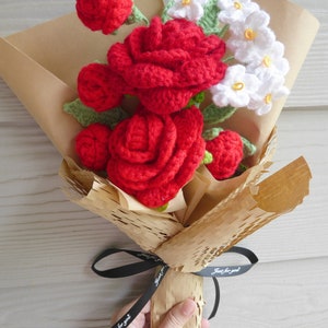 May include: A bouquet of crocheted flowers with large red roses and small white flowers with yellow centres. The flowers are wrapped in brown paper and tied with a black ribbon that reads "Just for you."