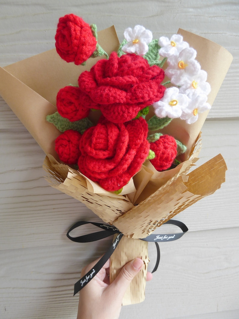 May include: A bouquet of crocheted flowers with large red roses and small white flowers with yellow centres. The flowers are wrapped in brown paper and tied with a black ribbon that reads "Just for you."