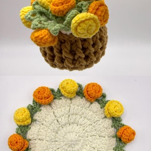 May include: A brown crocheted basket filled with yellow and orange flowers with green leaves, and a matching circular white crocheted doily featuring a border of alternating yellow and orange flowers with green stems and leaves.
