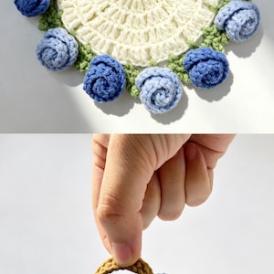 May include: A round, cream-colored crocheted coaster featuring a border of small, blue and light blue yarn roses with green leaves. Below, a small, brown crocheted basket is filled with several blue and light blue yarn roses and green leaves.