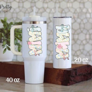 Puede incluir: Dos vasos aislados blancos con la palabra "MAMA" en colores pastel. El vaso m&aacute;s grande es de 1,18 litros y tiene un asa. El vaso m&aacute;s peque&ntilde;o es de 591 ml y tiene una pajita. Ambos vasos tienen un dise&ntilde;o floral y de lazo.