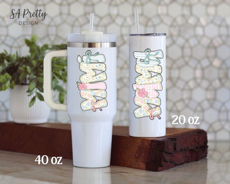 Puede incluir: Dos vasos aislados blancos con la palabra "MAMA" en colores pastel. El vaso m&aacute;s grande es de 1,18 litros y tiene un asa. El vaso m&aacute;s peque&ntilde;o es de 591 ml y tiene una pajita. Ambos vasos tienen un dise&ntilde;o floral y de lazo.