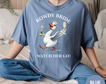 May include: A blue t-shirt with the text "ROWDY BRIDE" and a cartoon goose wearing a crown and veil, holding a champagne bottle and glass. The text "WATCH HER GO!" is below the goose.