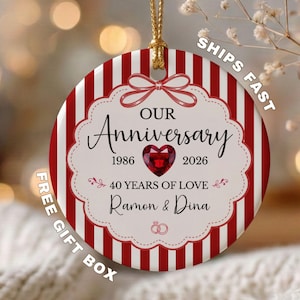 May include: A round ceramic ornament featuring red and white vertical stripes. The center displays a scalloped white frame with a red heart, the text "OUR Anniversary 1986 2026 40 YEARS OF LOVE Ramon & Dina," and a small line drawing of two rings.