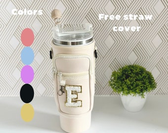 May include: A beige insulated tumbler holder with a zippered pocket and a white letter "E" with gold glitter. The holder is attached to a stainless steel tumbler with a clear lid. The image includes a free straw cover and a color chart with six different colors.