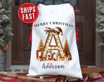 Puede incluir: Bolsa de regalo navideña blanca con cierre de cordón rojo. La bolsa presenta una gran letra "A" iluminada con un reno, árboles de Navidad y regalos. Las palabras "Merry Christmas" y "Addison" también están impresas.