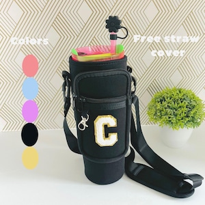 Puede incluir: Portavasos aislante negro con un bolsillo con cremallera y una correa. El portavasos tiene una letra "C" blanca y dorada en la parte delantera. El portavasos se muestra con opciones de color rosa, azul, morado, negro y amarillo.