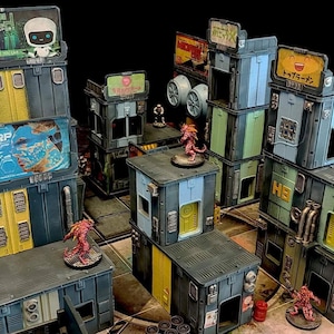 May include: Miniature, multi-level, industrial-themed terrain set. The structures are primarily gray with yellow, blue, and green accents. Signs with text are visible. Small, red figures are placed throughout the scene. The set is designed for tabletop gaming.