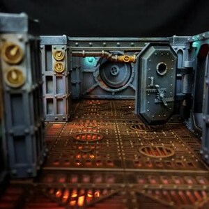May include: A detailed model of a futuristic, industrial-style corridor with metal walls and a grated floor. The walls are painted in shades of gray and blue, with accents of gold and green. The floor is a dark brown with a grid pattern. The corridor is lit by a soft, warm light. The text "Gothic Sector: Lost Ships" is visible at the top of the image.