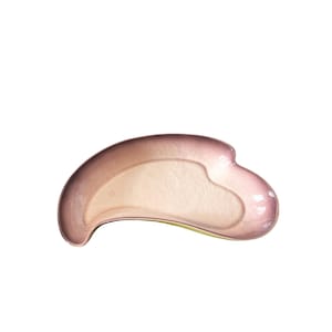 May include: A rose-colored, curved facial massage tool with a smooth, polished surface. The tool has a unique shape with rounded edges and a central indentation. The color gradient transitions from a darker pink to a lighter, almost translucent hue.