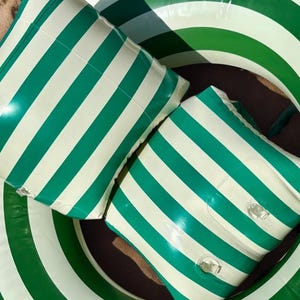 May include: An inflatable pool float set featuring a large circular ring and two square-shaped cushions, all decorated with a repeating pattern of bold emerald green and white vertical stripes made of a smooth, shiny, plastic material.