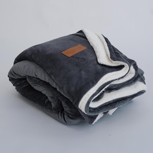 May include: A gray and white plush blanket is rolled up. The blanket has a brown leather tag with the text "KOZYUP" on it.