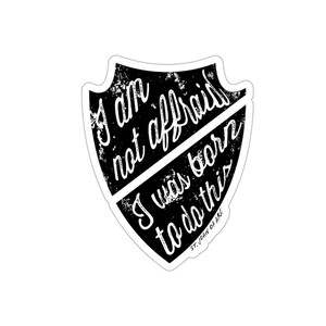 May include: Black and white sticker with a shield shape and the quote "I am not afraid I was born to do this" attributed to St. Joan of Arc.