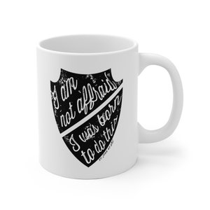 May include: White ceramic mug with a black shield design. The shield has the text "I am not afraid I was born to do this" and "ST. JOAN OF ARC".