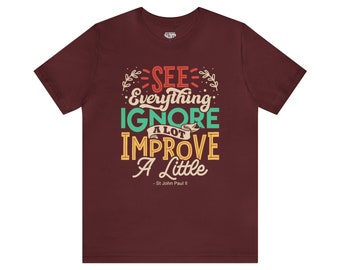 May include: A maroon t-shirt with a quote in a vintage style font that reads "See everything, ignore a lot, improve a little - St. John Paul II".