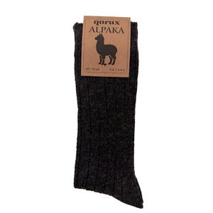 May include: A pair of dark charcoal grey ribbed socks with a textured knit finish. A brown cardboard tag is attached to the top, featuring the text qorux ALPAKA, an illustration of an alpaca, and the size information EU 39-42 and US 7.5-9.5.