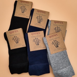 May include: Five pairs of socks in black, navy blue, and heather grey, each featuring a brown cardboard label with the text qorux bamboo collection, a bamboo stalk illustration, and the size 9-12 printed on the front of the packaging.