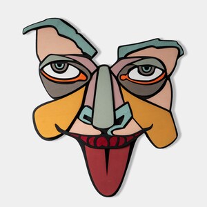 May include: A colorful, abstract face mask with a large, red tongue sticking out. The mask is made of paper and has a variety of geometric shapes and patterns.