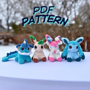 May include: Four crocheted plush toys in the shape of cartoon creatures are shown. The toys are in various colours, including blue, pink, beige, and green. The text "PDF PATTERN" is written in blue above the toys.