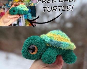 May include: A green crochet turtle with a shell in shades of yellow, green, and blue. The turtle has large, dark eyes and is held in a hand. The text "FREE BABY TURTLE!" is displayed above the turtle.