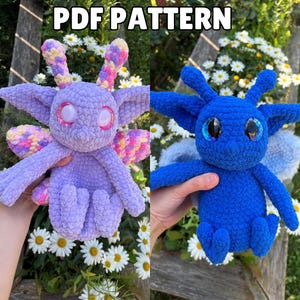 May include: PDF pattern for crocheting two amigurumi creatures. One is a purple and pink creature with large eyes and wings. The other is a blue creature with large eyes and wings. Both creatures are sitting on a bed of white flowers.