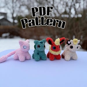 May include: Four crochet figures in various colours are shown, including a pink cat-like creature, a teal dinosaur-like figure, a red and yellow creature, and a cream-coloured cow-like figure. The words "PDF Pattern" are written above the figures.