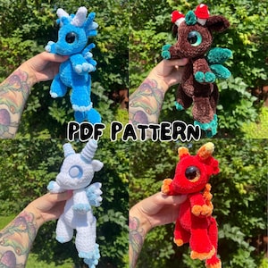 Puede incluir: Cuatro juguetes de dragón de ganchillo en azul, marrón, blanco y rojo. Cada dragón tiene características únicas, incluyendo cuernos, alas y diferentes acentos de color. El texto "PDF PATTERN" se muestra en la imagen.