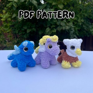 Puede incluir: Tres animales de peluche de ganchillo hechos a mano: un dinosaurio azul, un unicornio morado y un águila marrón y blanca. Cada uno tiene ojos grandes de color dorado. El texto "PDF PATTERN" está en la parte superior de la imagen.