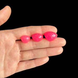 May include: Three pink heart-shaped resin beads with a glittery finish. The beads are arranged in a row from largest to smallest.