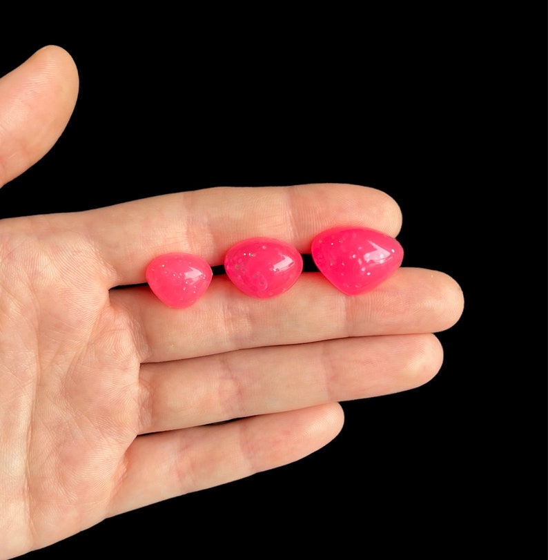 May include: Three pink heart-shaped resin beads with a glittery finish. The beads are arranged in a row from largest to smallest.