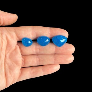 May include: Three blue resin cabochons of different sizes with a glittery finish. The cabochons are arranged in a row on a hand.