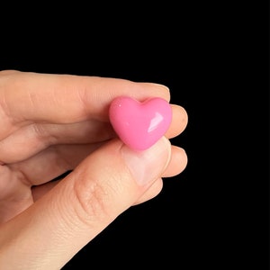 May include: A pink heart-shaped candy, held in a hand.
