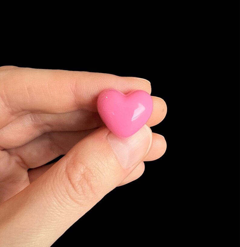 May include: A pink heart-shaped candy, held in a hand.