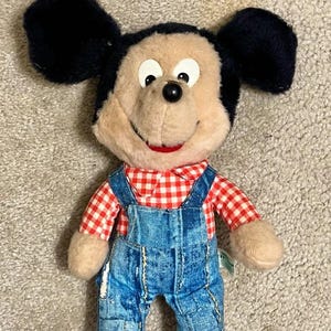 May include: A vintage plush Mickey Mouse toy wearing a red and white checkered shirt and blue denim overalls.