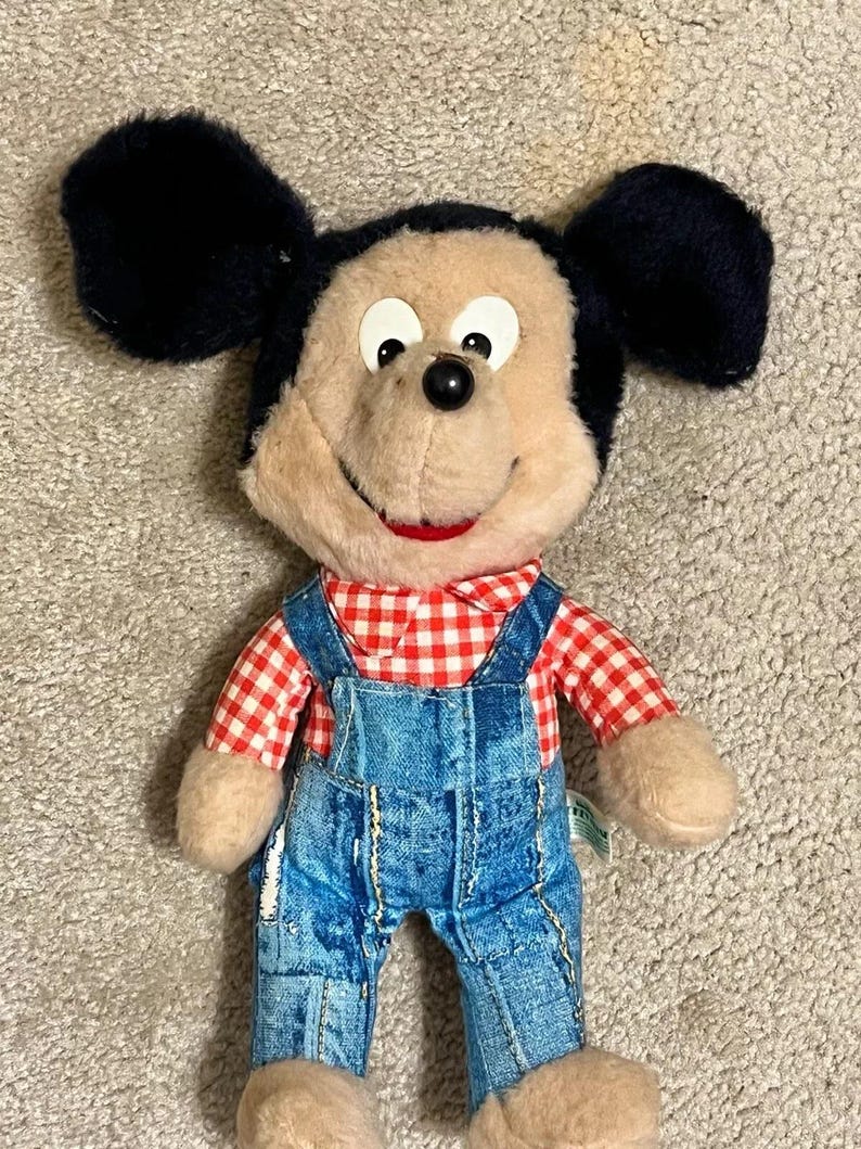 May include: A vintage plush Mickey Mouse toy wearing a red and white checkered shirt and blue denim overalls.