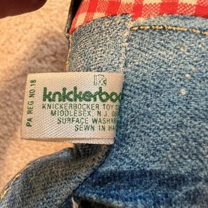 May include: A close-up of a green and white label with the text "Knickerbocker Toy Co. Middlesex, NJ 08846 Surface Washable Sewn in Haiti" on a denim stuffed toy.