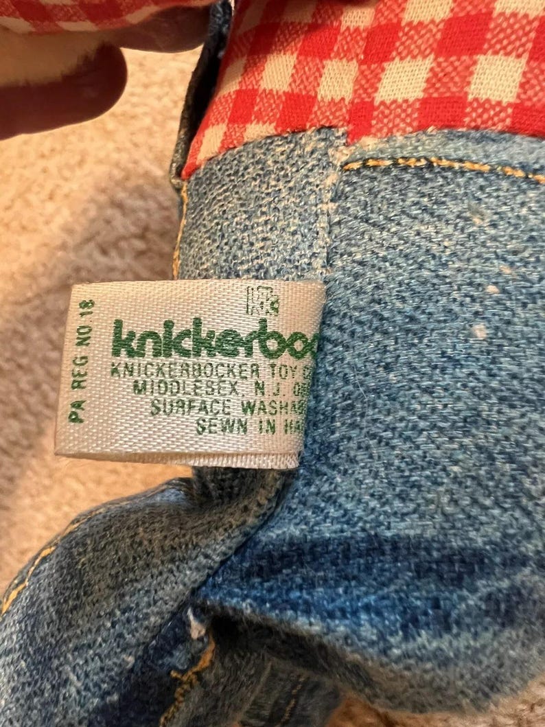 May include: A close-up of a green and white label with the text "Knickerbocker Toy Co. Middlesex, NJ 08846 Surface Washable Sewn in Haiti" on a denim stuffed toy.