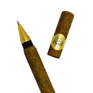 May include: A brown pen with a gold cap and a cigar-shaped design. The pen is in a closed position and the cap is off. The cap has a gold label with the text "Cigar Store" and a small image of a cigar.