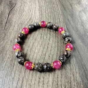 May include: A bracelet made of dark brown and black speckled beads with pink gemstone accents.