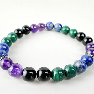 May include: A beaded bracelet featuring a variety of colorful gemstones. The bracelet includes black onyx, amethyst, malachite, and lapis lazuli beads. The beads are strung together with a silver-colored spacer. The bracelet is a stylish accessory.