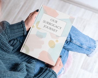 May include: A person is holding a book with a colorful abstract design and the text "Our Surrogacy Journey" on the cover.